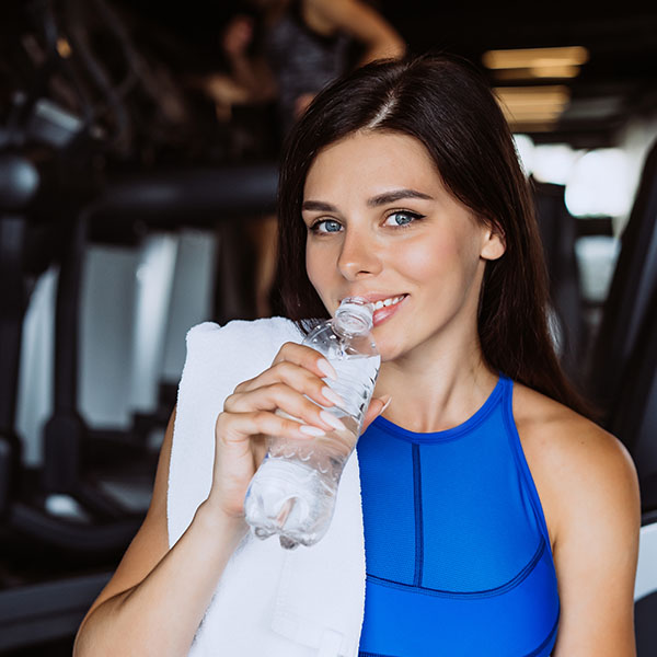 Vrouw met handdoek drinkend uit waterfles in sportschool.